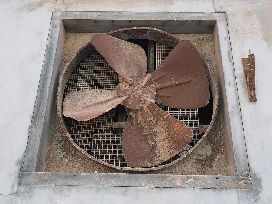 Old square exhaust fan with metal blades set into a wall opening