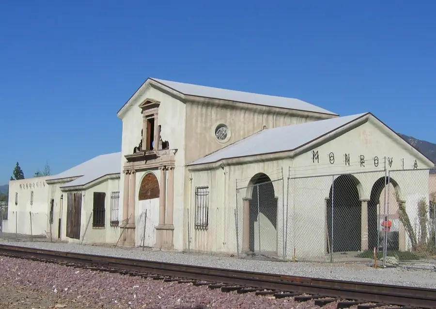 Historic Monrovia train station building with arched doors beside the railroad tracks