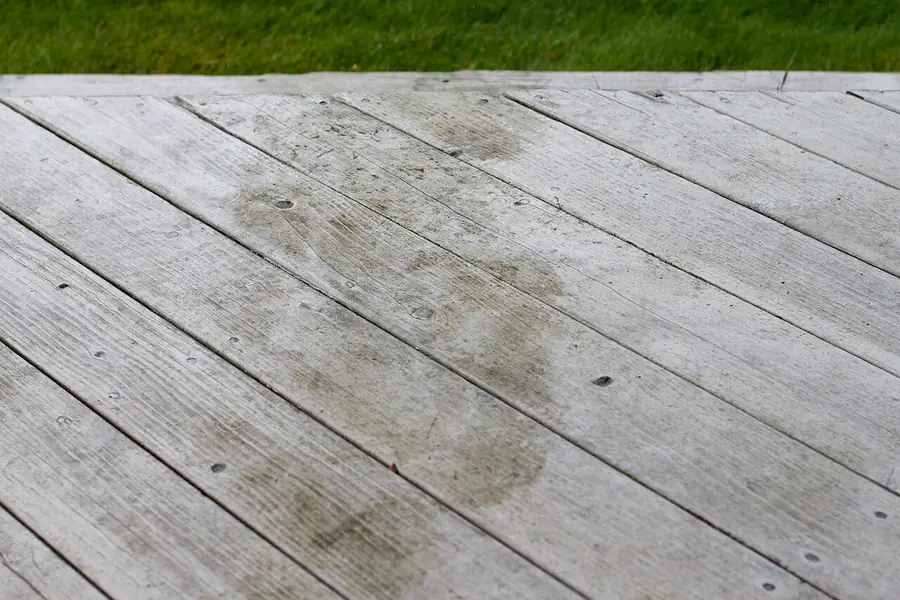 Gray weathered wood deck boards with dark wet patches after rain