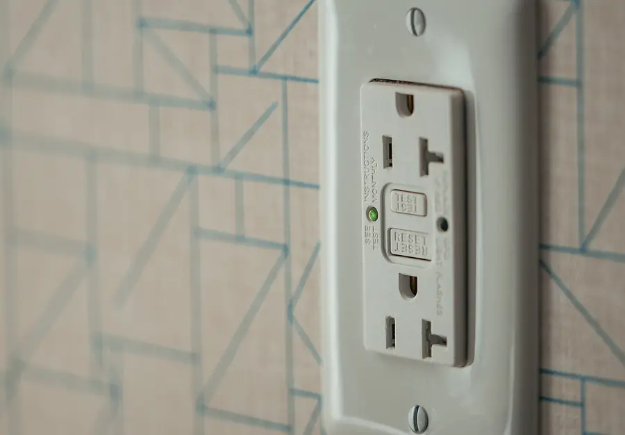 White GFCI outlet with TEST and RESET buttons on a patterned wall