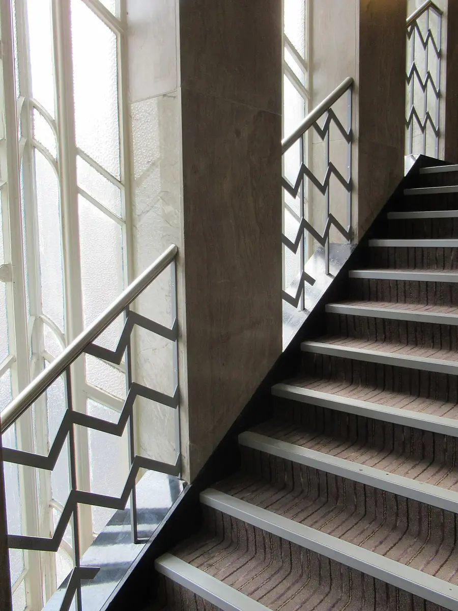 Staircase with a continuous metal handrail beside tall windows