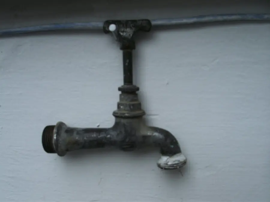Old metal outdoor water tap mounted on a pale painted wall