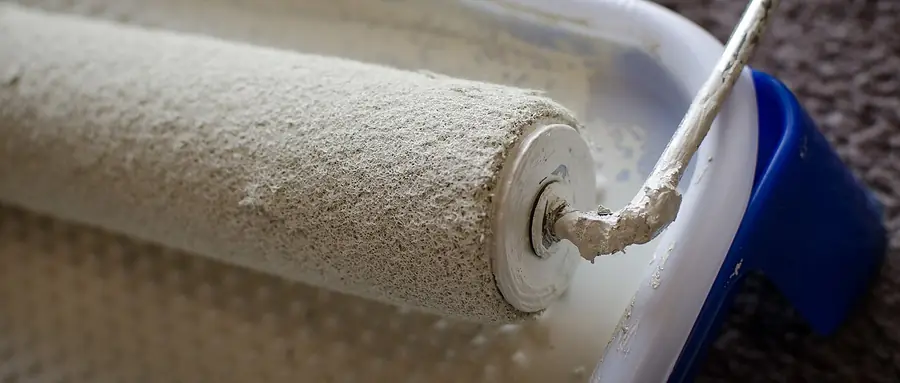 Paint roller on an extension pole against a wall