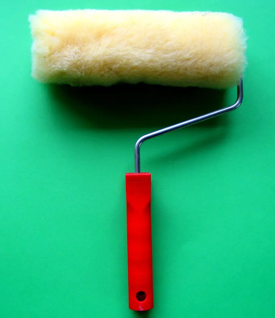 Paint roller with a fresh yellow cover and red handle on a green background