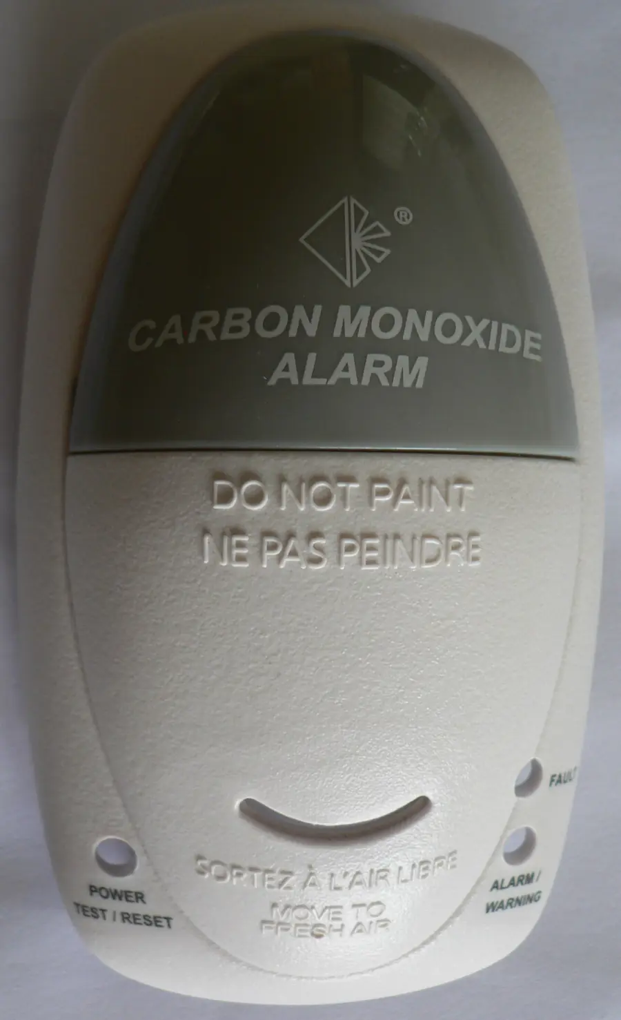 Gray carbon monoxide alarm mounted on a wall, seen up close