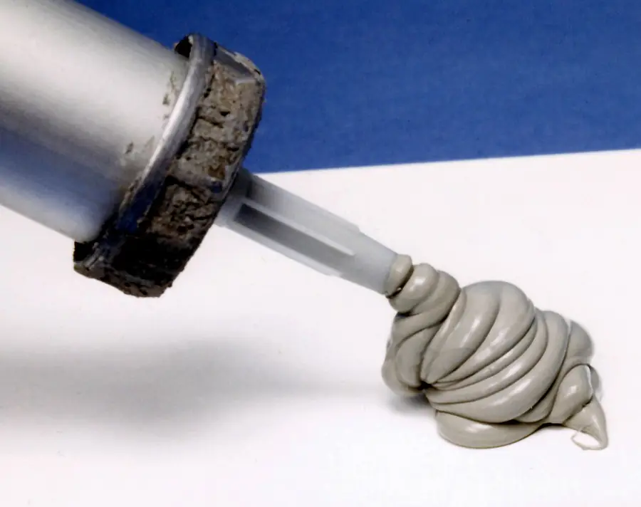 Caulking gun pushing out a thick bead of gray sealant from its nozzle