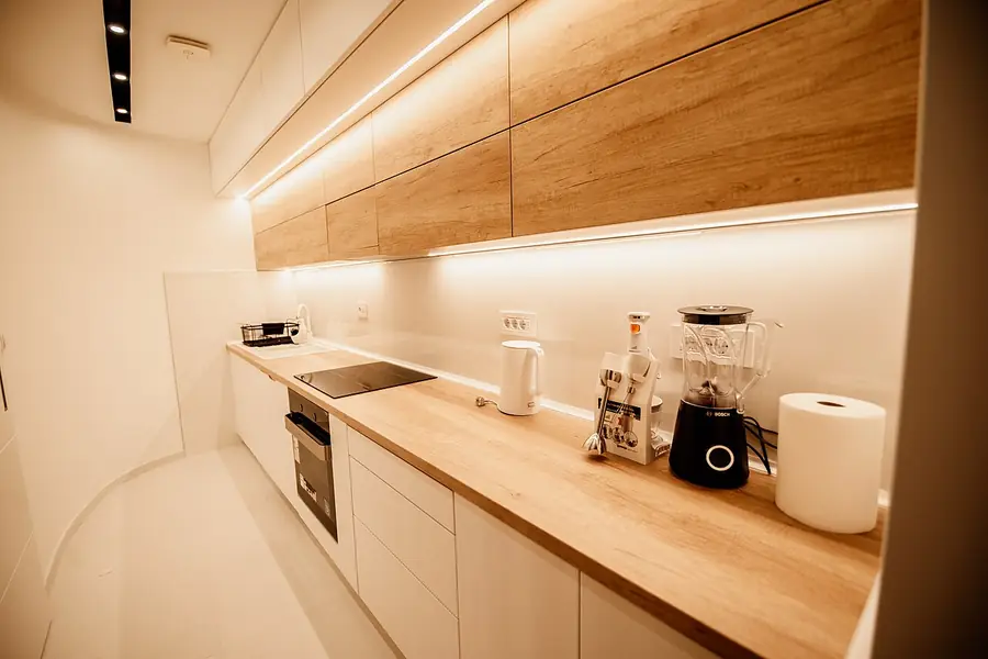 Kitchen counter lit by LED strip lights under light wood upper cabinets
