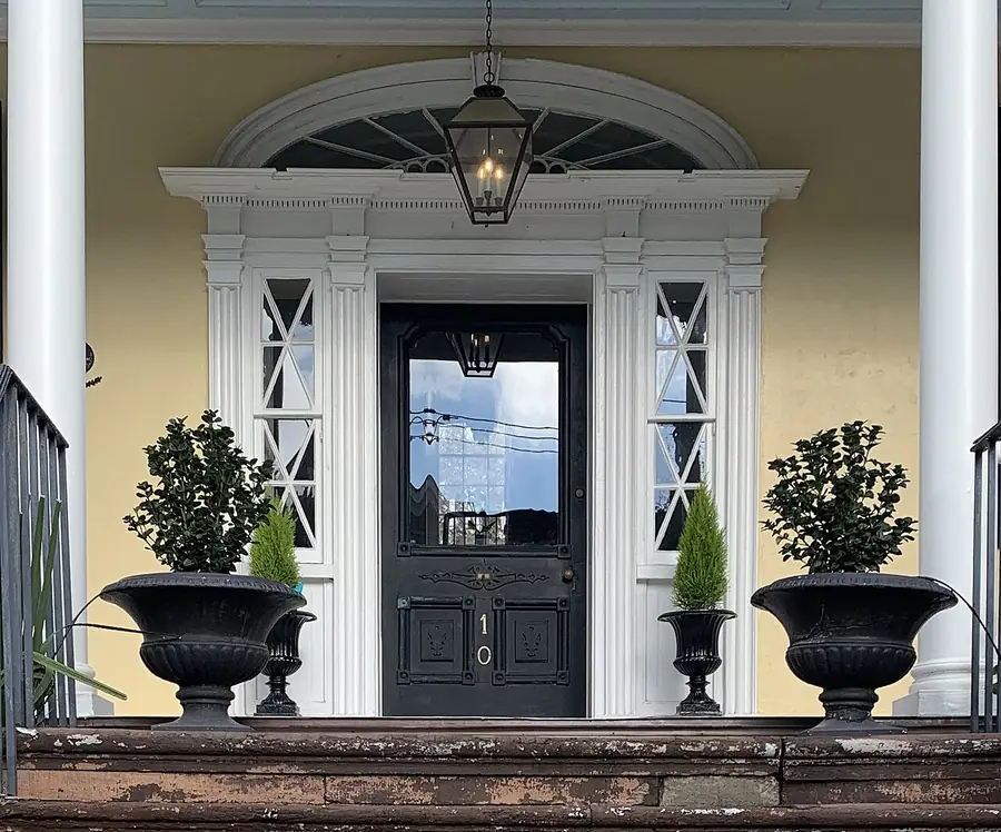 Black front door with glass sidelights and white columns on a yellow house