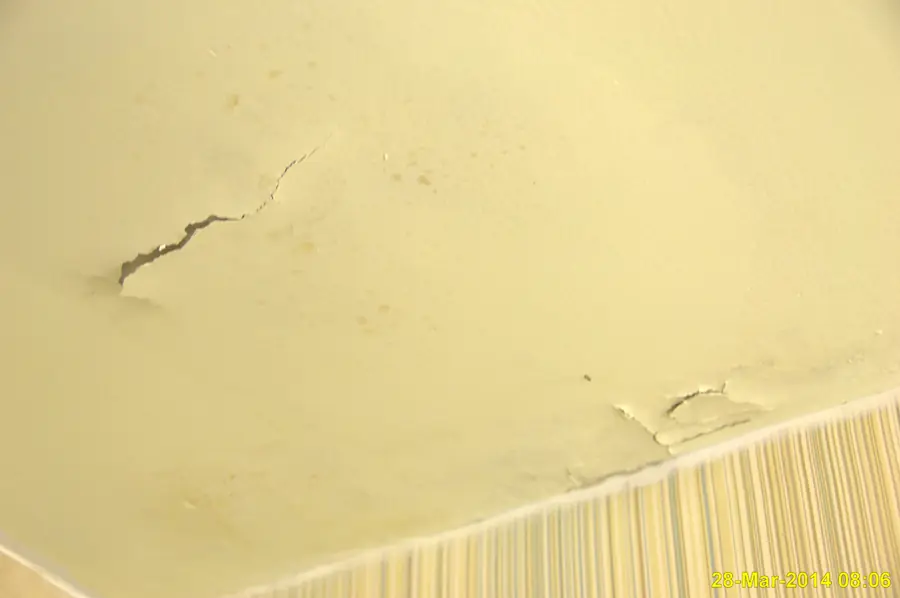 Yellow painted ceiling drywall with cracks and stains from water damage