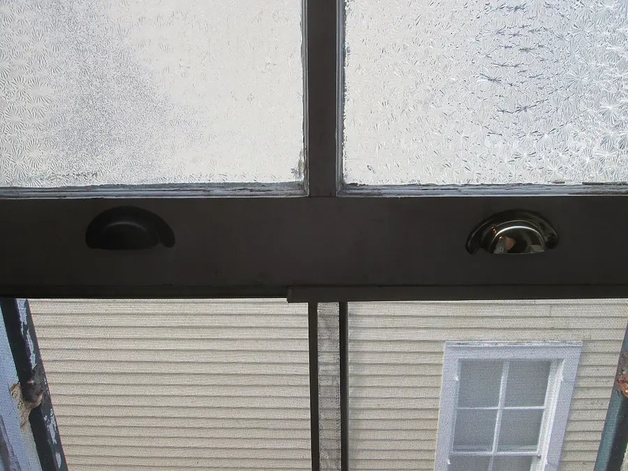 Window screen with a pull tab, seen from inside looking out at a house