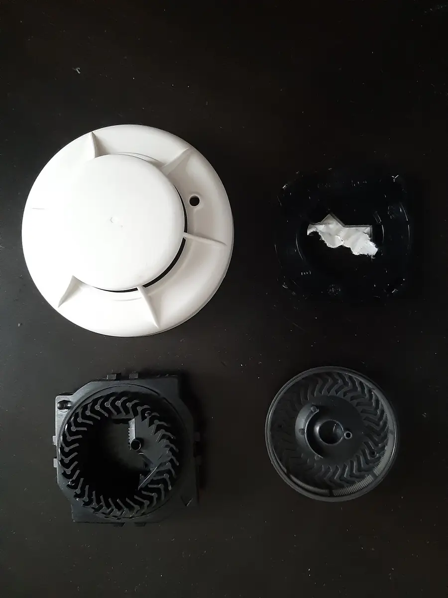 Two smoke detectors taken apart to show the sensor and battery parts