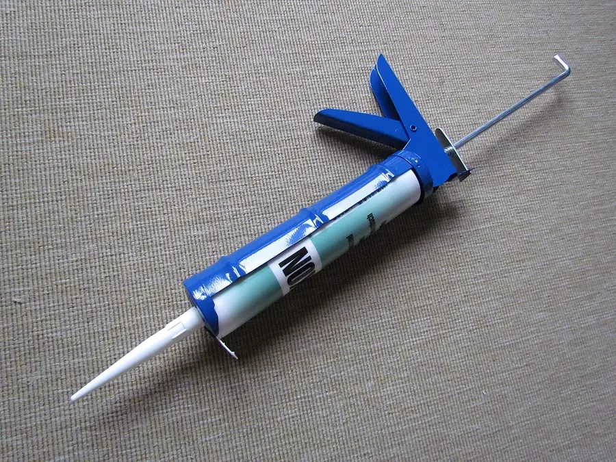 Blue caulking gun loaded with a sealant tube and a cut nozzle