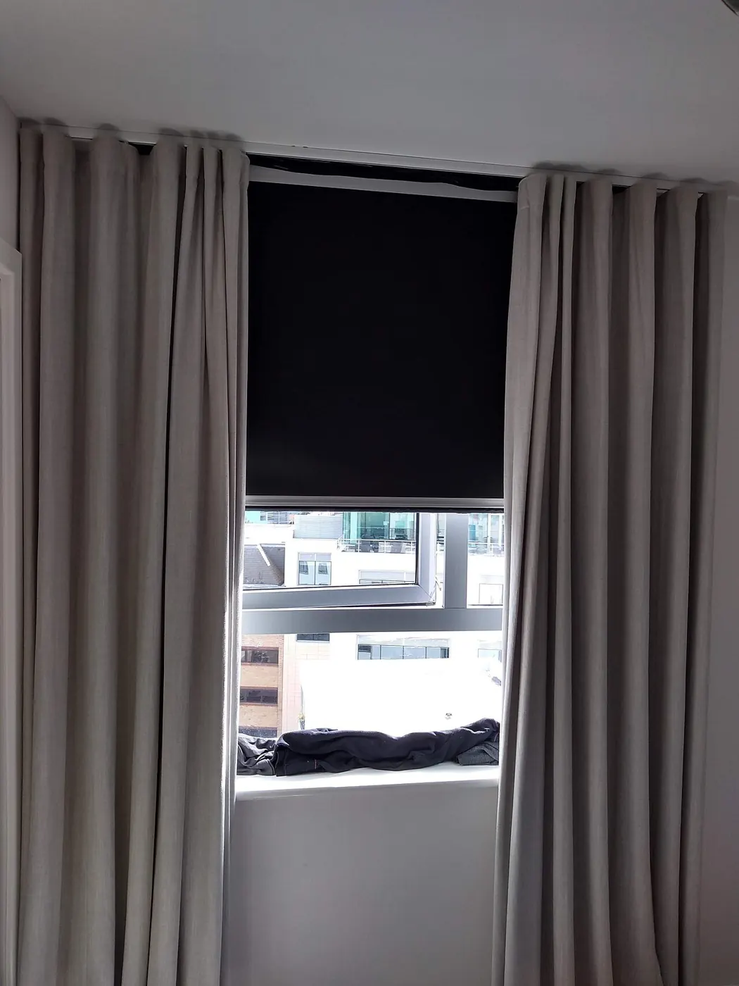Window fitted with a roller blind between floor-length curtains