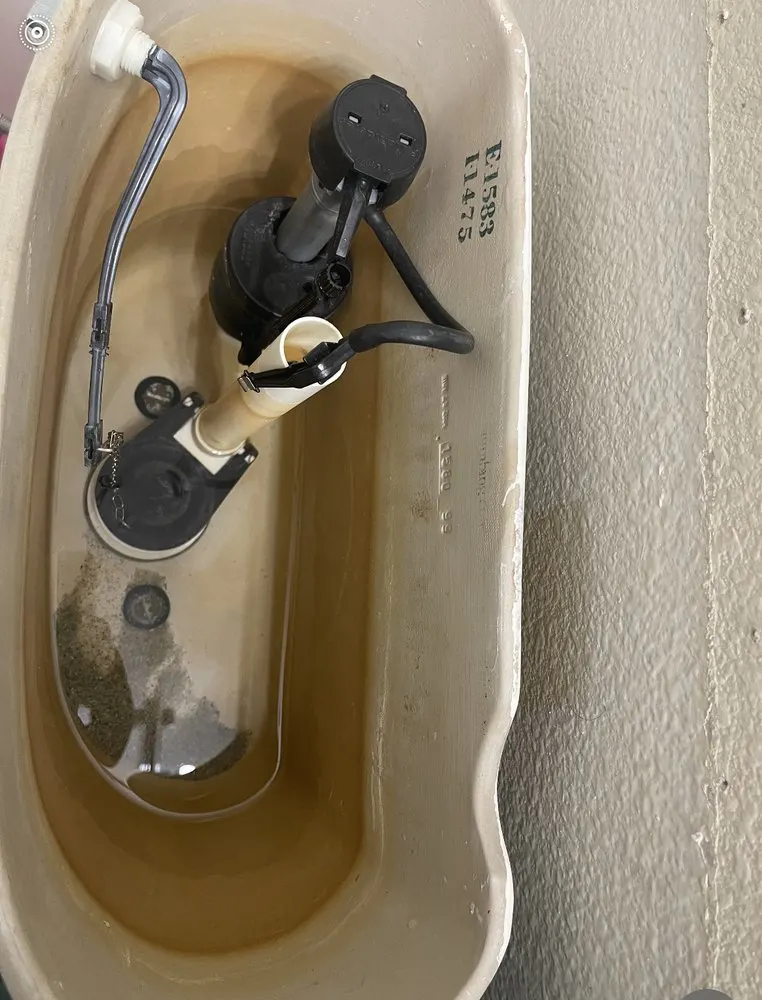 Inside a toilet tank showing the fill valve and stained flush parts