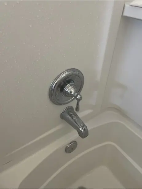 Tub and shower trim with a single-handle valve and spout on a white wall