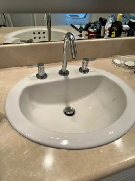 Chrome bathroom faucet over a white oval sink in a stone counter