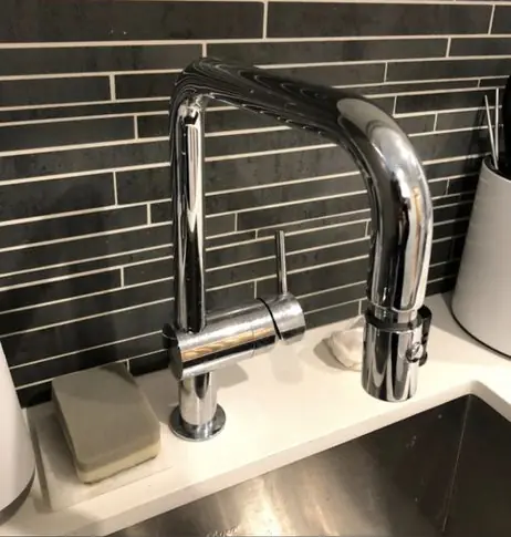 Chrome pull-down kitchen faucet installed against a glass tile backsplash