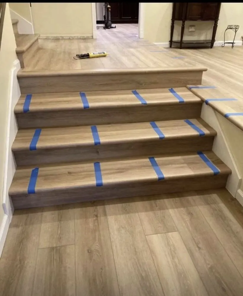 Stair treads being covered with vinyl plank, held with blue tape while the adhesive sets