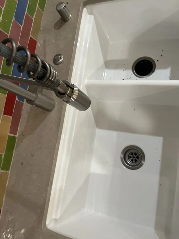 Chrome faucet over a white double-bowl sink with colorful glass tile behind