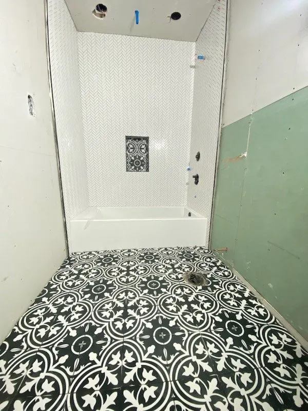 Black-and-white patterned floor tile in a small bathroom with a new tub surround