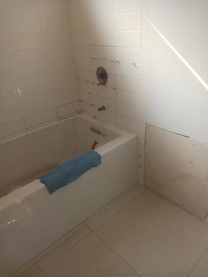 Tub surround and tub edge before new caulk, with blue tape marking the line