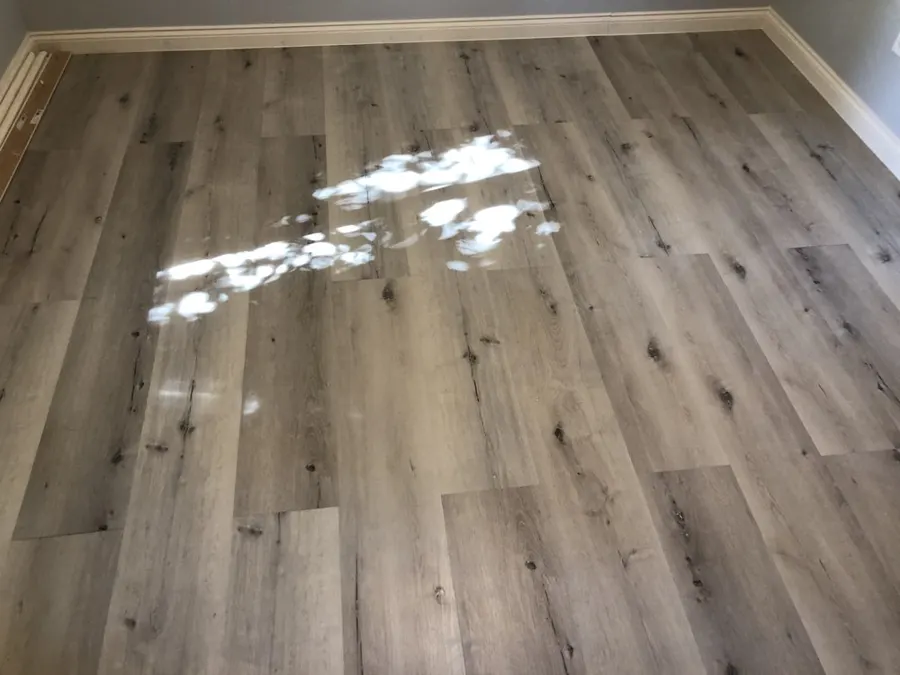Bedroom floor finished in gray vinyl plank with sunlight across it